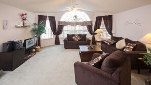 A living room with a brown sofa, a TV, and a ceiling fan. - Ip60497 - Island Club West - 3 Bed 2 Baths Condo (Kissimmee)