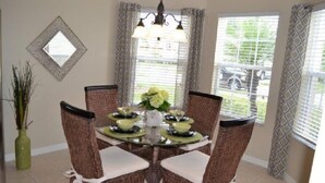 A dining area with a round glass table, wicker chairs, a chandelier, and a view of the outdoors through large windows. - Ip60503 - The Shire at West Haven - 4 Bed 3 Baths Villa (Davenport)