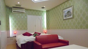 A hotel room with a bed, a red sofa, a white table, and a painting on the wall. - HOTEL MOULIN ROUGE - Adults Only (Ibaraki)