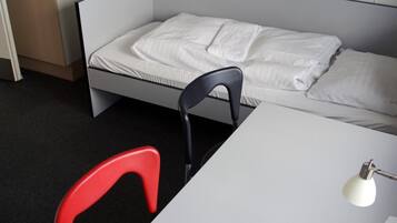 Ein Einzelbett mit weißer Bettwäsche, ein roter Sessel, ein weißer Schreibtisch, eine Lampe und eine Fernbedienung.