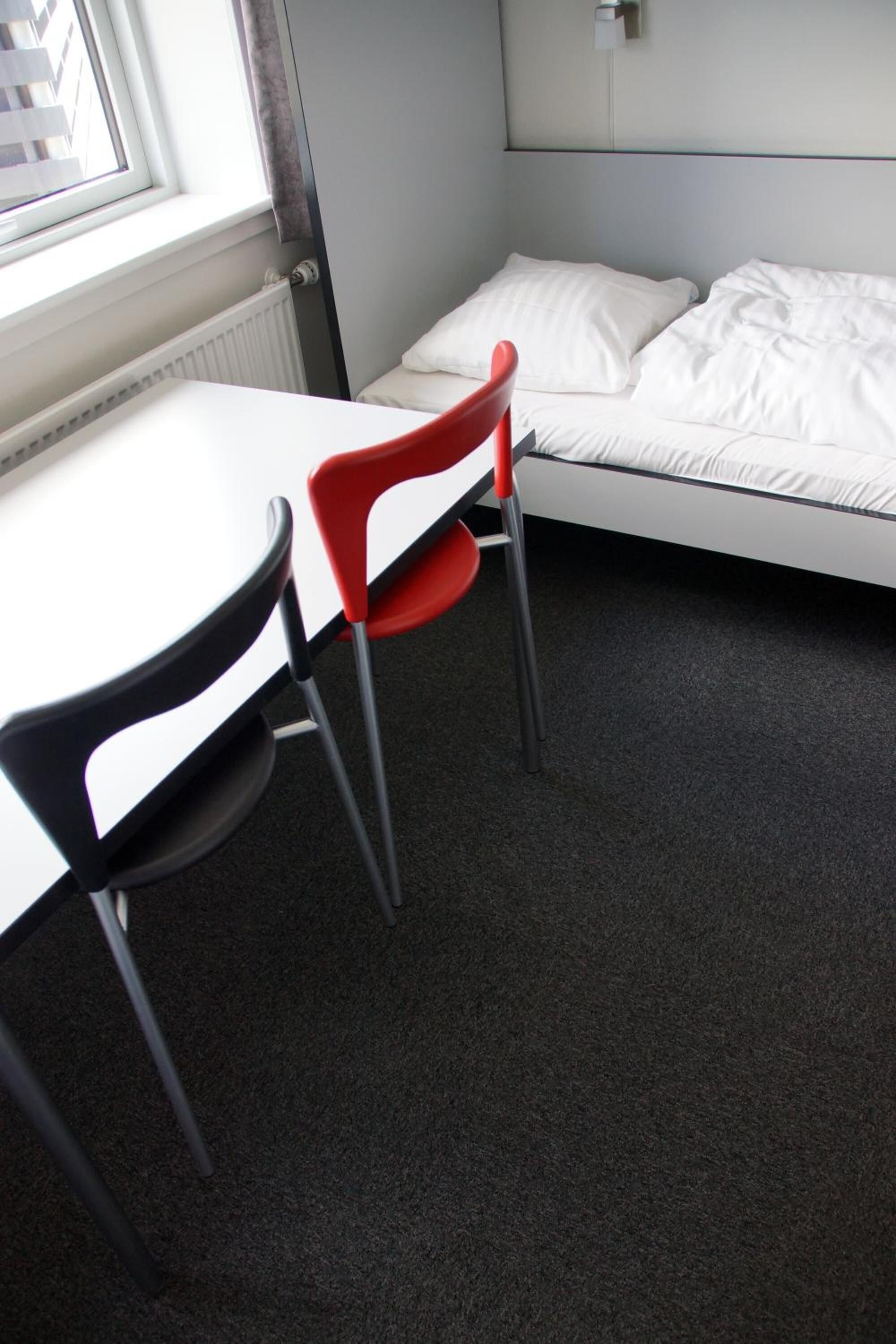 A small room with a single bed, a table, and two chairs.