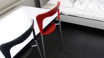 Una habitación pequeña con una cama individual, una mesa y dos sillas.