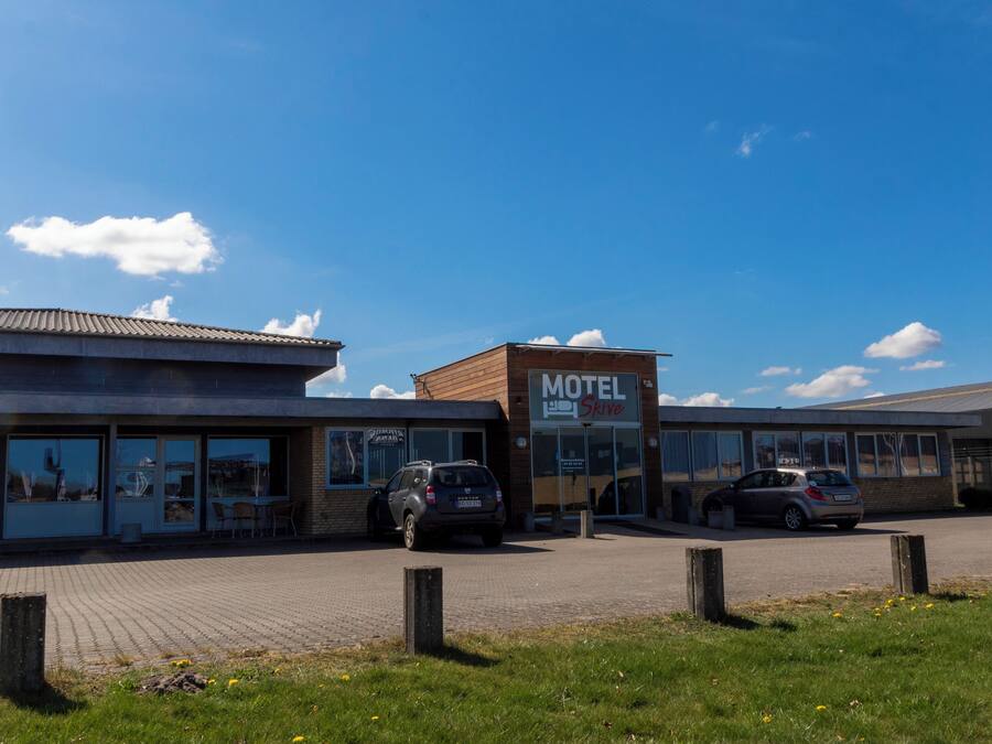 A motel with a clear blue sky, a parking lot, and a grassy area in front.