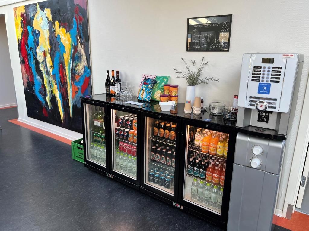 A beverage refrigerator with various drinks, a payment terminal, and a colorful abstract painting on the wall.