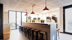 A modern bar area with a central island, bar stools, red pendant lights, and potted plants. - Student Factory Bordeaux (Bordeaux)