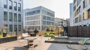 A rooftop patio with a round wooden table, white chairs, and green cushions. - Student Factory Bordeaux (Bordeaux)