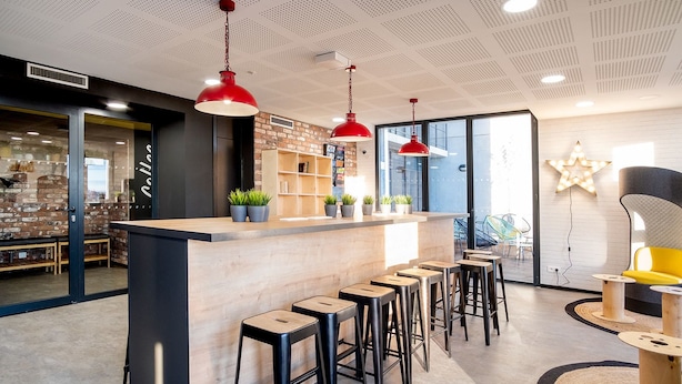A modern bar area with a wooden counter, black stools, and red pendant lights. - Student Factory Bordeaux (Bordeaux)
