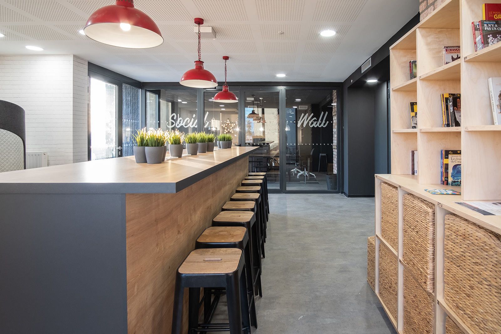 Un área de bar moderna con una barra alargada, taburetes e iluminación colgante roja.