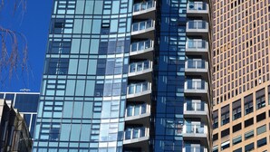 A tall, modern glass building with multiple balconies and a clear blue sky in the background. - Executive Stay on Little Collins (Melbourne)