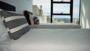 A bed with white bedding and striped pillows, a window with a cityscape view, and a modern architectural design. - Executive Stay on Little Collins (Melbourne)