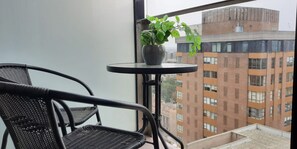 Un balcón con una silla de mimbre y una pequeña mesa con una planta en maceta.