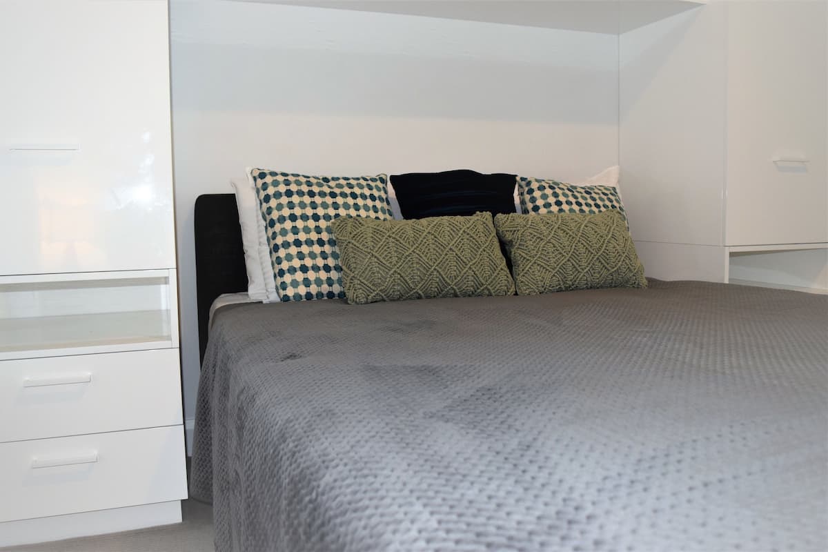 Un dormitorio con cama, armario blanco y almohadas estampadas.