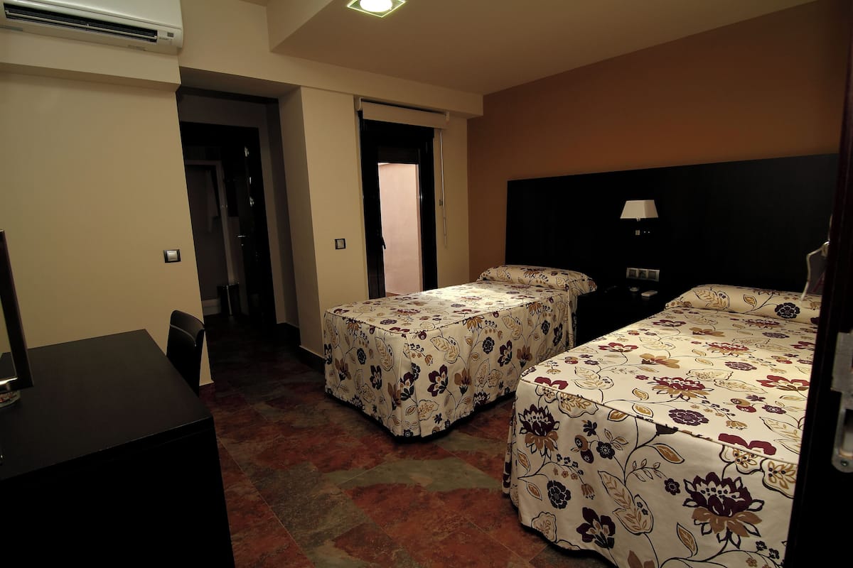 Habitación de hotel con dos camas, un escritorio y una silla. Se ve una puerta que da a otra habitación.