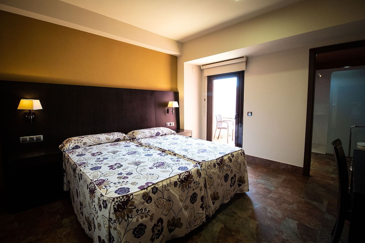 Habitación de hotel con cama doble, dos lámparas de noche, una mesita y una silla.