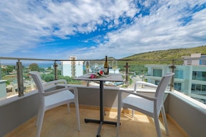 Un balcon avec une table et des chaises, offrant une vue sur le paysage urbain et les collines.