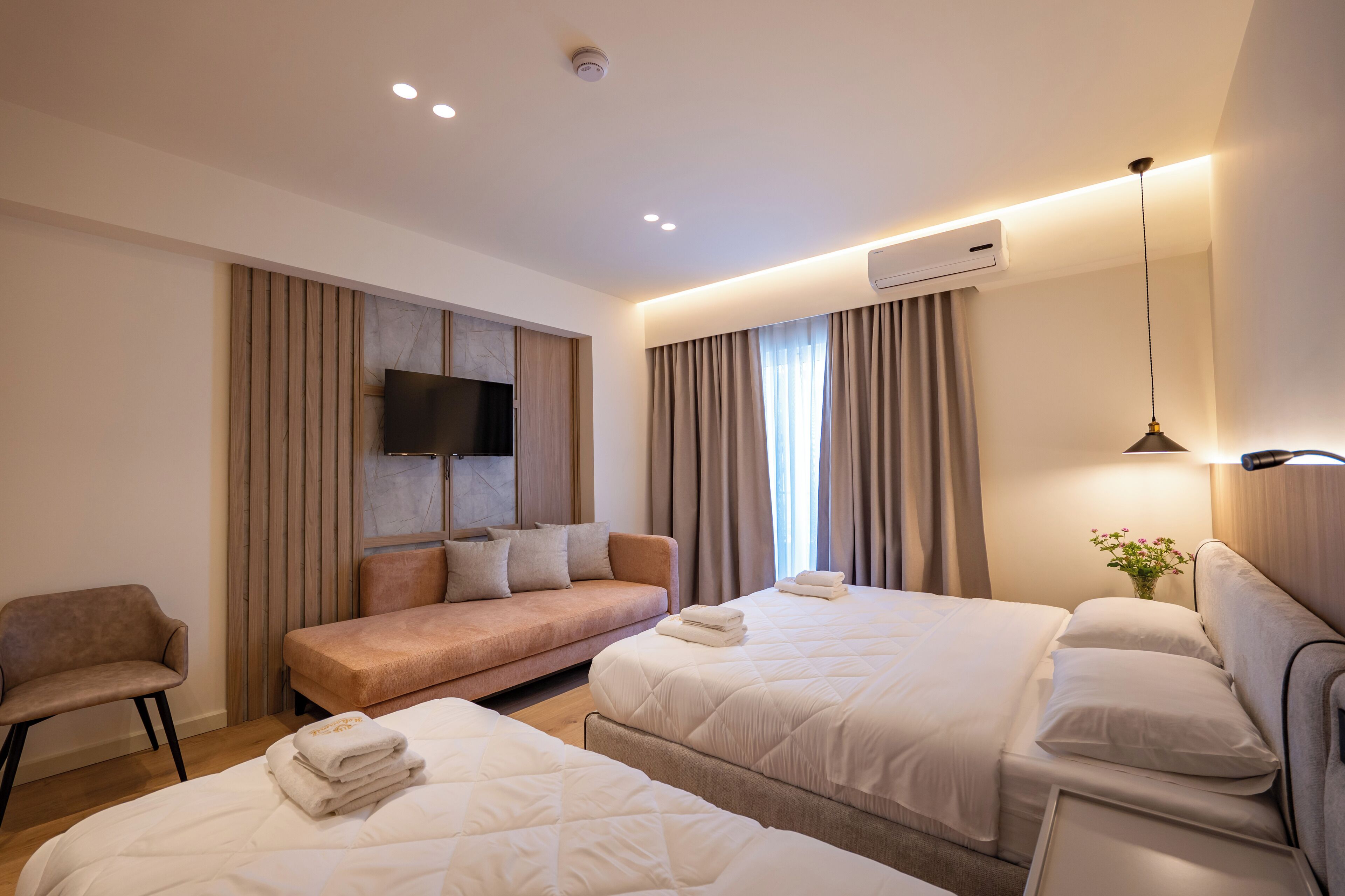 Quarto de hotel com duas camas, um sofá, uma TV e um aparelho de ar condicionado.