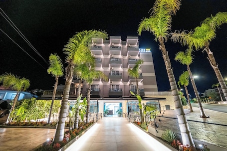 A modern hotel with a central courtyard, surrounded by palm trees and a well-lit entrance.