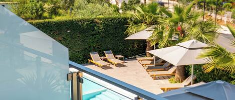 A balcony with a marble table and chairs, overlooking a swimming pool area with lounge chairs and umbrellas.
