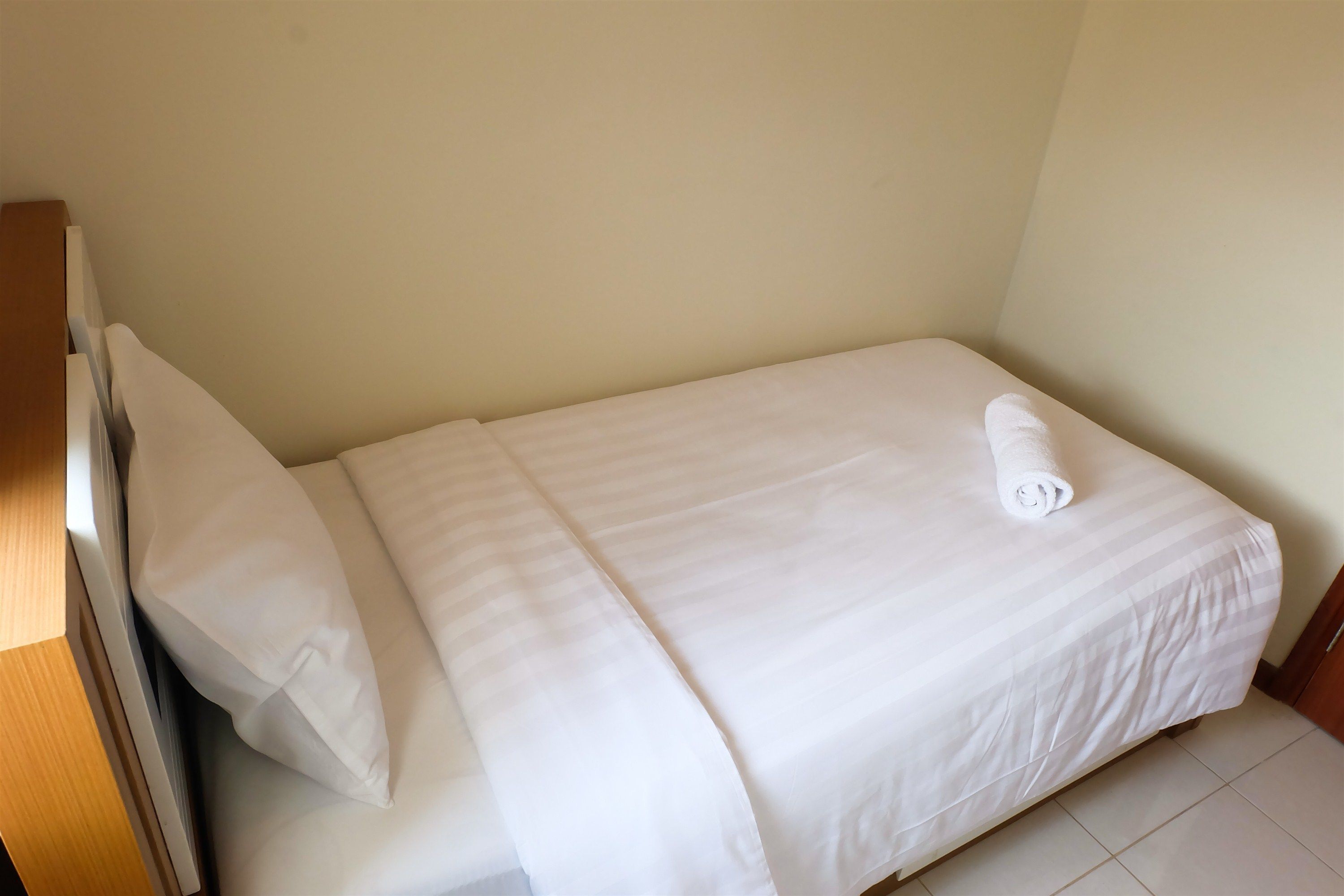 A single bed with white bedding and a rolled towel on it.