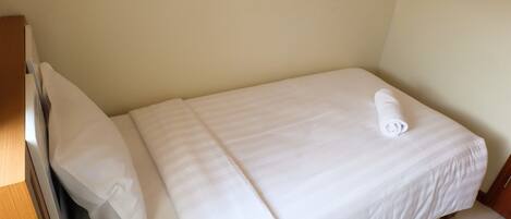 A single bed with white bedding and a rolled towel on it.