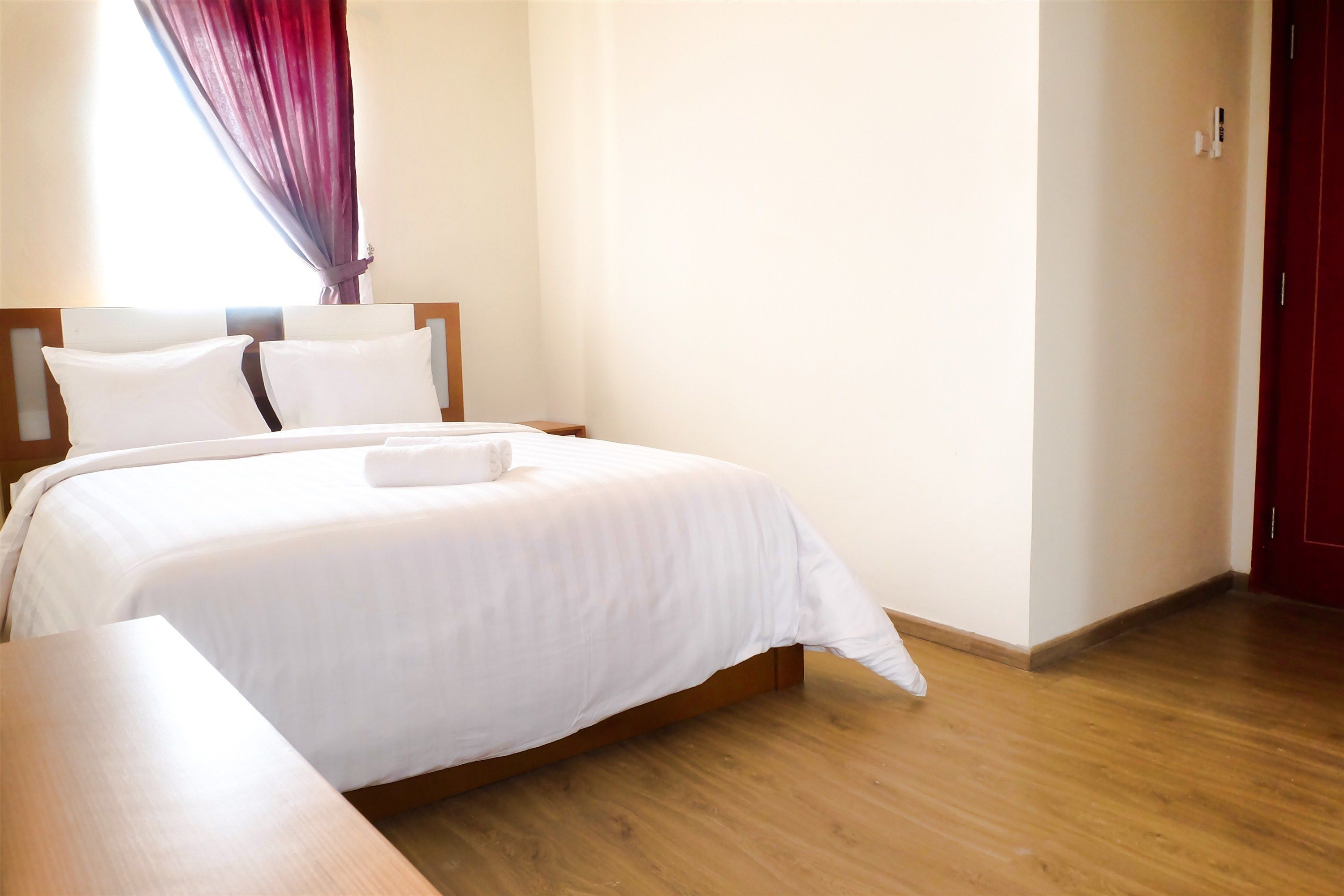 A neatly made bed with white linens and pillows, a wooden headboard, and a wooden floor.