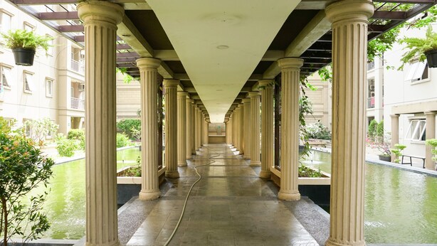 A corridor with columns, a water feature, and hanging plants. - Grand Palace Kemayoran Apartment For Lifestyle Living (Jakarta)