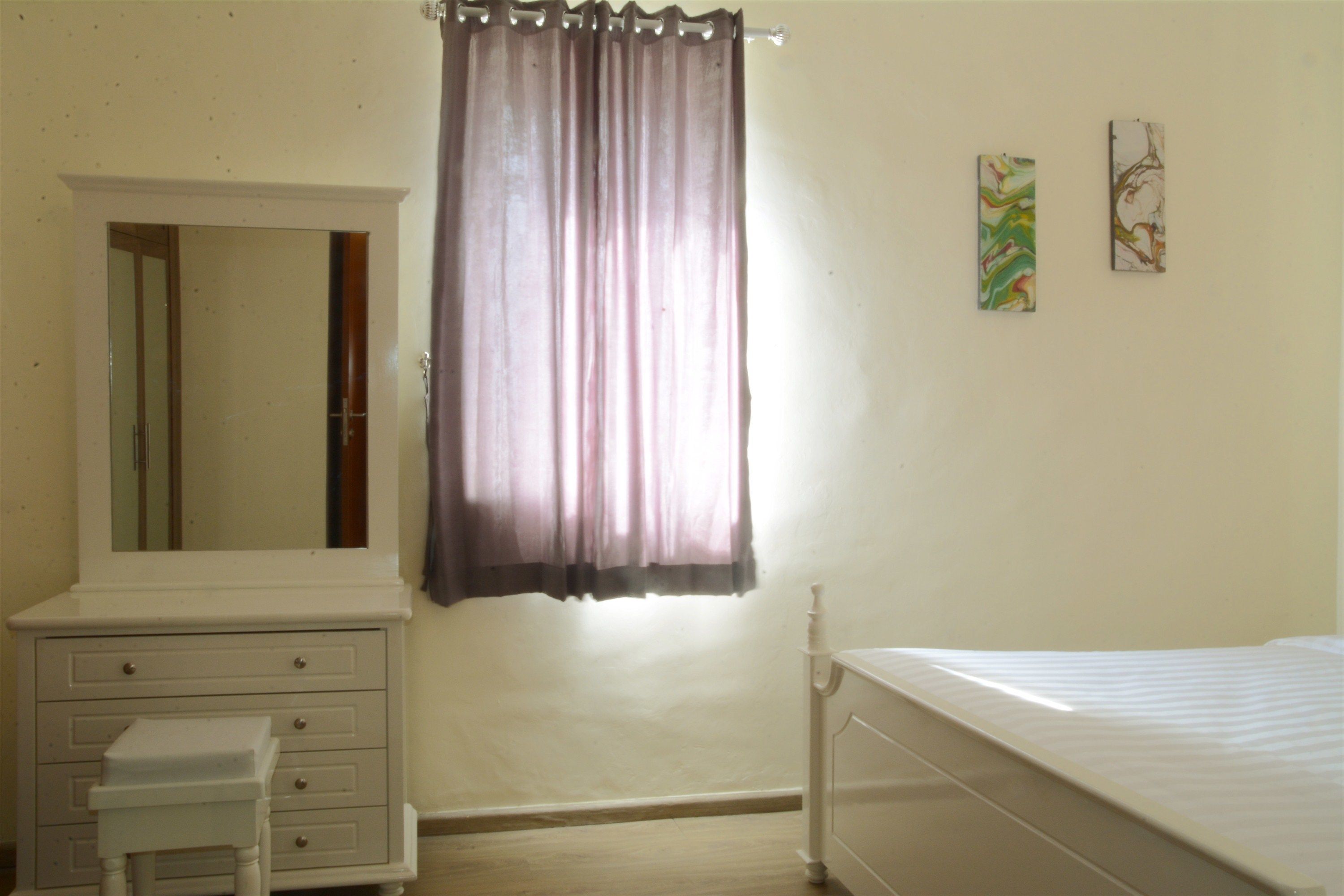 A bedroom with a bed, a dresser, a mirror, and a window with curtains.