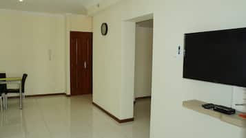 Een woonkamer met een flatscreen televisie aan de muur, een houten deur, en een eethoek met een tafel en stoelen.