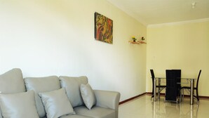 A modern living room with a grey sofa, a glass coffee table, and a dining area with a table and chairs. - New And Modern Grand Palace Kemayoran Apartment (Jakarta)