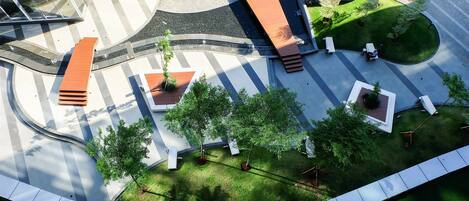 An aerial view of a modern public space with a curved pathway, seating areas, and greenery.
