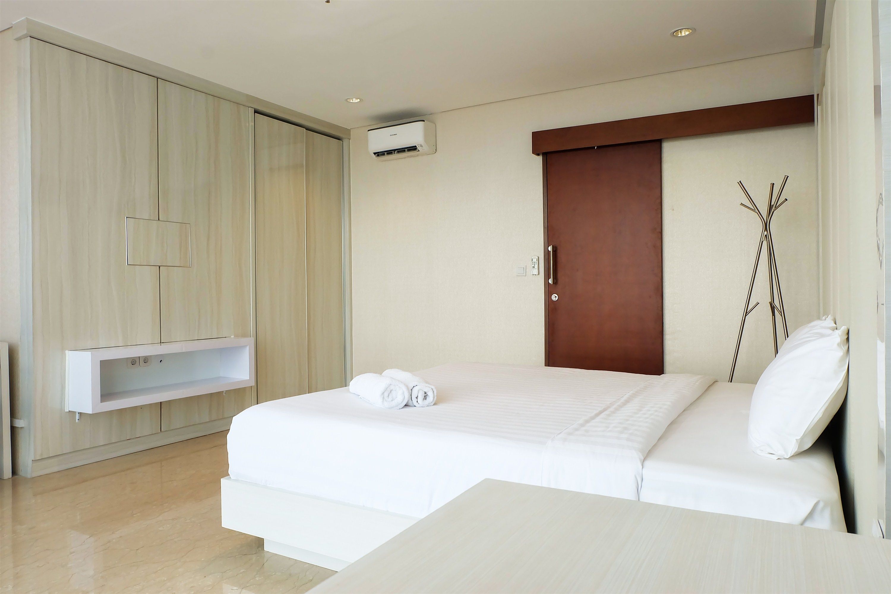 A hotel room with a bed, a wardrobe, a built-in shelf, and an air conditioning unit.