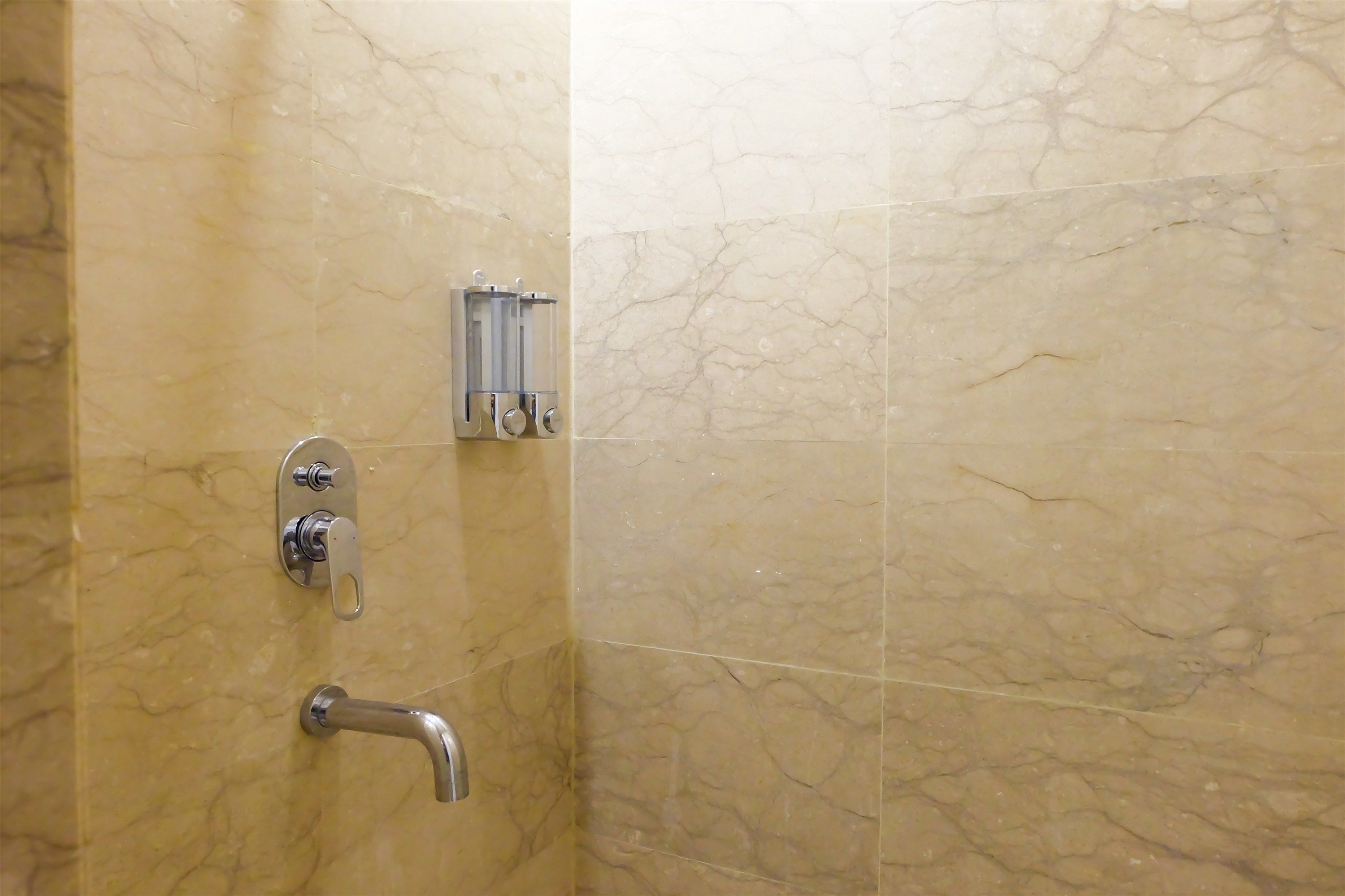 Un baño con paredes de mármol, una ducha con cabezal de ducha de mano y un perchero para toallas.