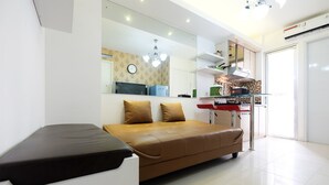 A modern living room with a sofa, a glass coffee table, and a kitchen area with a refrigerator, microwave, and stove. - Affordable Bassura City Apartment (Jakarta)