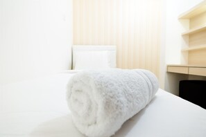 A neatly made bed with a rolled white towel, a white pillow, and a wooden headboard. - Affordable Bassura City Apartment (Jakarta)