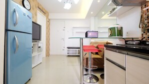 A modern kitchen with a blue refrigerator, a glass bar stool, and a television. - Affordable Bassura City Apartment (Jakarta)