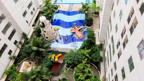 An aerial view of a hotel courtyard with a swimming pool, palm trees, and a small waterfall. - Affordable Bassura City Apartment (Jakarta)