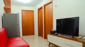 Ein Hotelzimmer mit einem roten Sofa, einem Fernseher auf einer Holzkommode, einem Kühlschrank und zwei Holztüren.