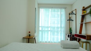 Ein Hotelzimmer mit Bett, Schreibtisch, Stuhl, einem kleinen Tisch mit Vase und einem Fenster mit durchsichtigen Vorhängen.