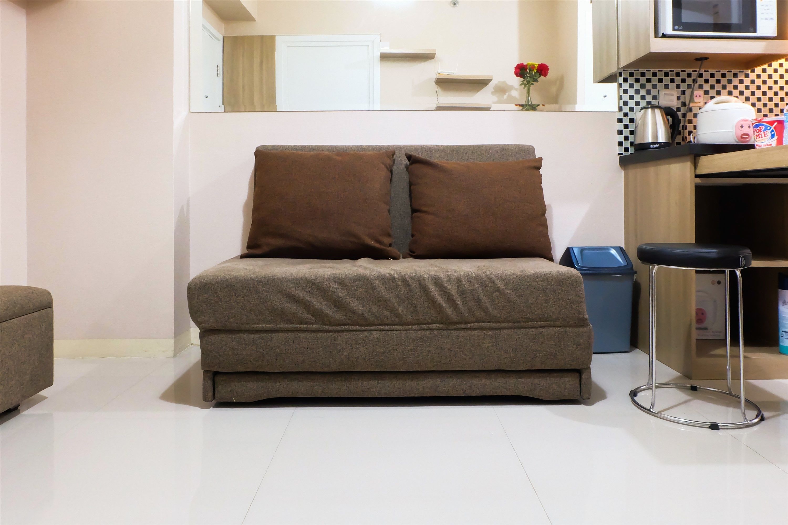 A small, modern living area with a sofa, a stool, and a kitchen counter with appliances.