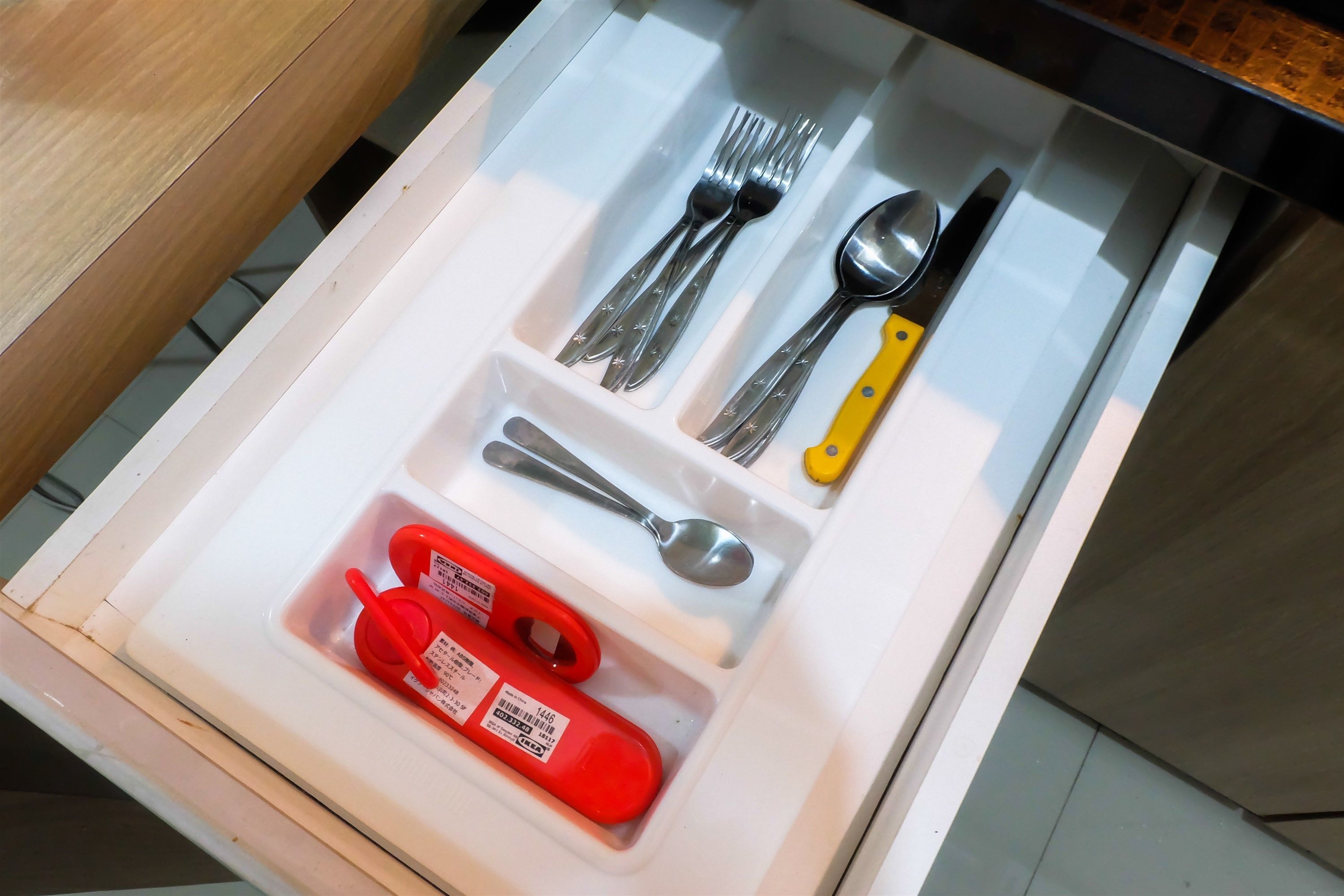 A drawer with utensils and a red bottle.