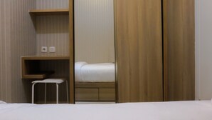 A hotel room with a bed, a small stool, a shelf with two electrical outlets, and a wooden wardrobe.