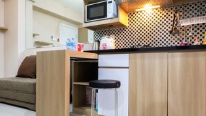 A compact kitchen with a microwave, kettle, and a small stool.