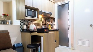 A compact kitchen with a microwave, kettle, and bar stools.