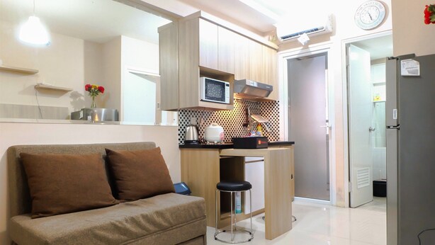A compact kitchen with a microwave, stove, and a small bar stool. A sofa with brown cushions is positioned in front of the kitchen.