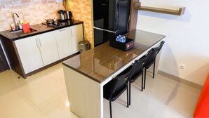 Una cocina moderna con una isla de vidrio, sillas negras, un refrigerador y una cafetera.