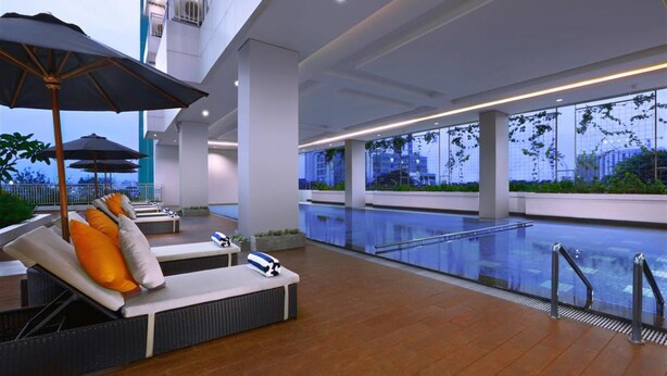 Un área de piscina interior moderna con sillones de descanso y sombrillas, ventanas amplias y vistas a la ciudad.