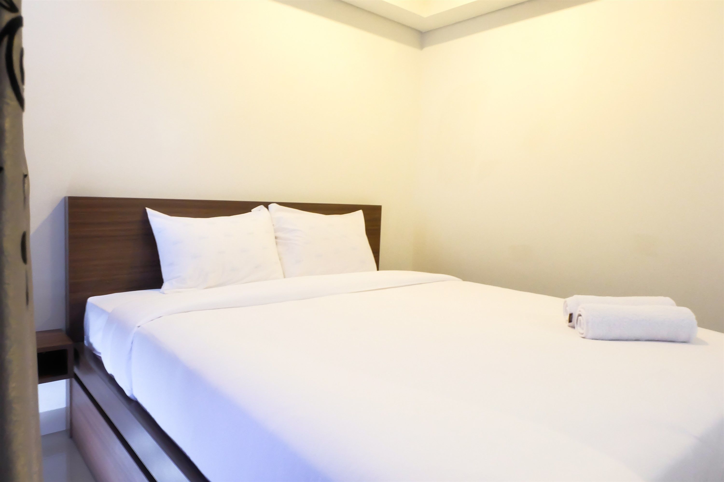 A neatly made bed with white linens and pillows, a wooden headboard, and a rolled towel on the bed.