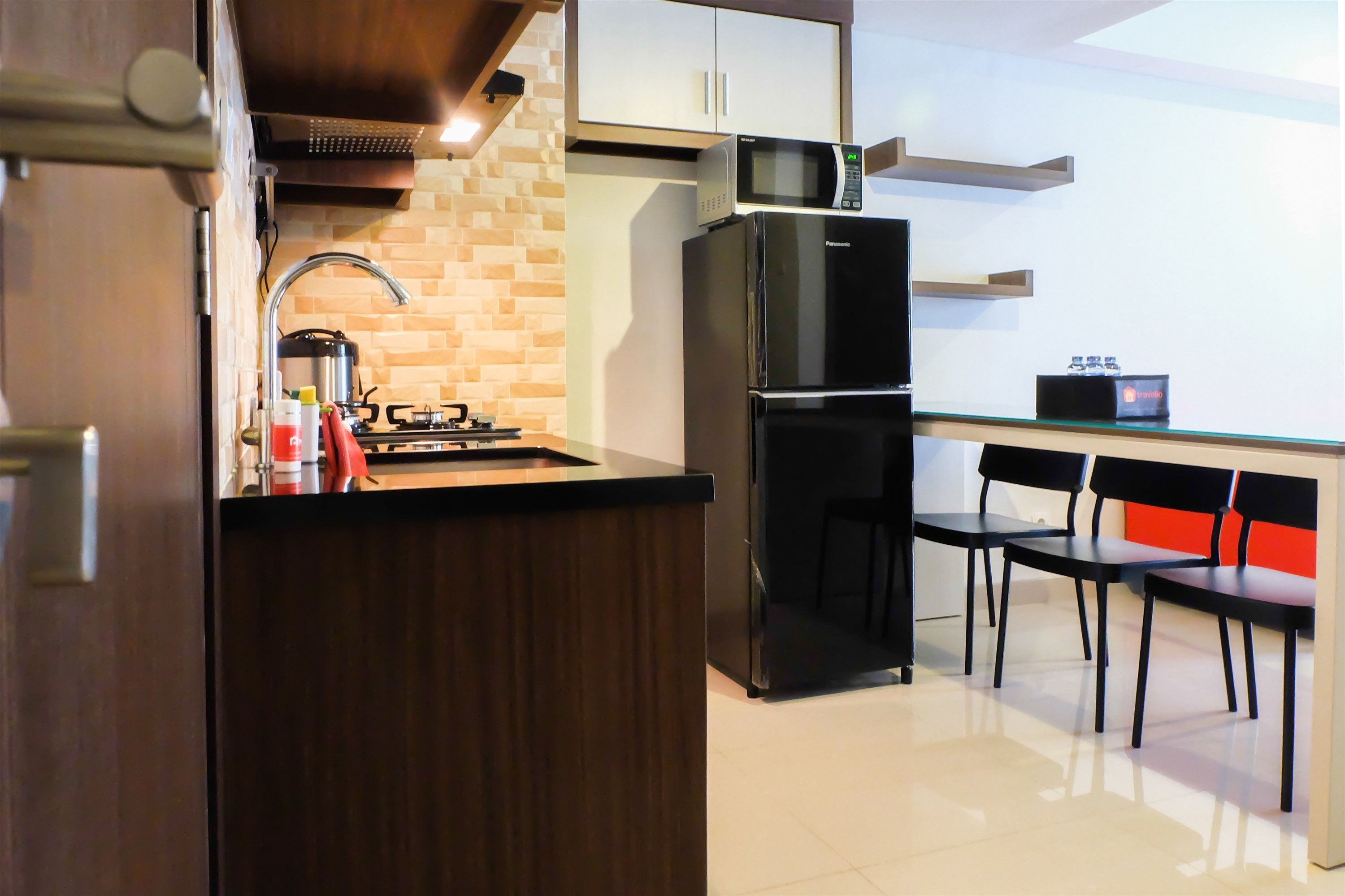 Cocina compacta con microondas integrado, un refrigerador negro, estufa a gas y un lavamanos. Hay dos sillas negras y una mesita.