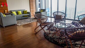 Een moderne woonkamer met een grijze bank, twee fauteuils, een salontafel en een groot raam met uitzicht op de stad.