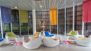 Een moderne loungehoek met witte wicker meubels, kleurrijke kussens en een decoratieve vaas in het midden.